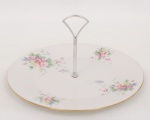 Royal Doulton, Stoke-on-Trent - Inglaterra(Fundada em 1805 por John Doulton). Prato para doces ou petit-four em porcelana inglesa, padrão Summer Bouquet, decoração floral policroma distribuída em reservas sobre fundo branco, borda com filete dourado e alça central em metal cromado. Marca da manufatura no verso. Medidas: Alt.: 13 x Diam.: 27 cm.
