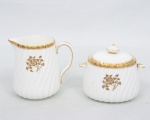Minton, Staffordshire - Inglaterra. Um(01) açucareiro e uma(01) leiteira em porcelana inglesa da década de 1950, padrão Gold Rose. Esmaltagem vítrea de tom branco perolado, realçado por profusa ornamentação com flores, faixas e filetes à ouro. Bojo ricamente modelado com frisos em espiral relevados na própria pasta, tampa encimada por pega com feitio de pião, bico vertedor revirado para fora, alça da leiteira em voluta, e alças do açucareiro em forma de folhagems estilizada revirada para baixo. Marca da manufatura ao fundo. Medidas: Açucareiro: Alt.: 10,5  x Comp.: 13 x Larg.: 9,5 cm. Leiteira: Alt.: 11,5  x Comp.: 13 x Larg.: 9 cm.