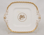 Minton, Staffordshire - Inglaterra. Exuberante bandeja em porcelana inglesa da década de 1950, padrão Gold Rose. Esmaltagem vítrea de tom branco perolado, realçado por profusa ornamentação com flores, faixas e filetes à ouro. Formato retangular, de quinas arredondadas, modelado com frisos em espiral, e alça laterais integradas em folhagens, relevados na própria pasta. Marca da manufatura ao fundo. Medidas: Comp.: 25 x Larg.: 21,5 cm.