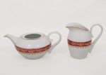 Porcelana Schmidt - Brasil(Fundada em 1945). Um(01) bule para chá(sem tampa) e uma(01) leiteira em porcelana nacional da década de 1960/70; esmaltagem vítrea na cor branca, decorado com faixas de tom rubi e ornamentação em douradura aplicada, formando cercaduras de arabescos, elementos fitomorfos e rendilhados estilizados; bordas contornadas por filetes à ouro, bico vertedor do bule curvado, da leiteira ondulado e revirado para fora, alças laterais em voluta. Marca da manufatura no verso. Medidas: Bule: Alt.: 11 x Comp.: 25 x Larg.: 16 cm. ; Leiteira: Alt.: 14,5 x Comp.: 16 x Larg.: 10 cm.