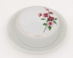 Porcelana Renner, Porto Alegre - RS(Fundada em 1937). Manteigueira em porcelana nacional da década de 1960/70, série "Medaillon"; esmaltação branca, decorada por composição floral em estampagem policromada, cercada por friso em douradura. Marca da da manufatura ao fundo. Medidas: Alt.: 6 x Diam.: 17,5 cm.