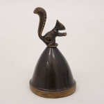 Sino de mesa em metal patinado, corpo cônico e empunhadura escultórica representando esquilo estilizado. Contém badalo interno metálico. Medidas: Alt.: 9 x Diam.: 5 cm.