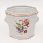 Ernesto & Hugo Saler , Guarulhos - SP (Ativo nas décadas 50/60). Cachepot octogonal em porcelana branca moldada em relevo, com aplicações de mascarões leoninos laterais, decoração floral policromada em reservas e frisos dourados. Marca da manufatura ao fundo. Medidas: Alt.: 13,5 x Diam.: 17 cm.