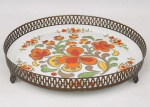 Porcelana Schmidt - Brasil(Fundada em 1945). Bandeja circular em porcelana, aba decorada por composição floral estilizada em policromia, em tons de laranja, amarelo, verde e castanho, montada em estrutura vazada de metal. Marca da manufatura no verso. Medidas: Alt.: 6 x Diam.: 32,5 cm.