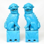 Elegante par de esculturas representando cães de fó, executadas em cerâmica cobertas com esmaltagem vítrea na tonalidade azul turquesa, dotados de rica ornamentação modelada em relevo. Apresentam-se com postura tradicional, bocas abertas com a língua para fora, um com uma das patas apoiadas sobre esfera vazada, e outro em cima de um filhote; ambos assentados sobre base alta de formato retangular. Medidas: Alt.: 42 x Comp.: 18 x Larg.: 10 cm.