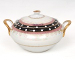 Porcelana, Steatita e Magnésia S/A, Campo Largo - PR (fundada em 1954). Sopeira em porcelana nacional da década de 1960/70; corpo bojudo ornamentado em composição concêntrica. Borda em esmalte preto ornada por reservas circulares em branco, intercaladas de maneira ritmada, contornada por filetes dourados. Faixa subsequente em esmalte rosa com sequência de grinaldas e elementos fitomorfos estilizados aplicados em douração. Corpo e tampa com acabamento nacarado e motivos radiais estilizados em ouro brunido. Alças laterais em arcos vazados e revirados para cima, com acabamento dourado. Tampa de perfil abaulado com pega central em formato de flor, igualmente dourada. Contorno ondulado com acabamento dourado aplicado à borda. Marca da manufatura ao fundo. Medidas: Alt.: 16 x Comp.: 27 x Larg.: 22 cm.