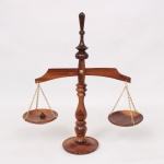Balança decorativa de mesa em madeira torneada, composta por coluna central com remate em pináculo, travessa arqueada e dois pratos suspensos por correntes metálicas, assente sobre base circular. Medidas: Alt.: 31,5 x Comp.: 28,5 cm.