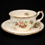 W.H. GRINDLEY, Staffordshire - Inglaterra(Fundada por William Harry Grindley em 1880). Xícara para chá em faiança inglesa da década de 1940/50, padrão "Creampetal"; esmaltagem de tom marfim, decoração floral policroma com reservas de rosas e flores campestres distribuídas pelo bojo e caveto, aplicada por transferência. Bordas recortadas com acabamento em douradura, repetido na asa lateral em voluta. Marca da manufatura no verso. Medidas: Xícara: Alt.: 5,5 x Comp. 11,5 x Larg.: 9 cm; Pires: Diam.: 14,5 cm.