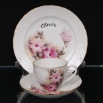 Trio para chá em porcelana, composto por xícara, pires e prato de pão, com decoração floral policromada pintada à mão em tons de rosa e sépia, bordas moldadas em relevo e filetes dourados. Apresenta monograma ao centro do prato, vide foto. Medidas: Xícara: Alt.: 6,5 x Comp.: 10,5 x Larg.: 8 cm. ; Pires: Diam.: 14,5 cm. ; Prato: Diam.: 20 cm.