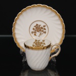 Minton, Staffordshire - Inglaterra. Excepcional xícara para café em porcelana inglesa da década de 1950, padrão Gold Rose. Esmaltagem vítrea de tom branco perolado, realçado por profusa ornamentação com faixas e filetes à ouro, fundo interno contendo flor em reserva. Bojo aproximadamente cilíndrico com alça lateral em voluta, ricamente modelado com frisos em espiral relevados na própria pasta; padrão decorativo replicado no pires. Marca da manufatura no verso. Medidas: Xícara: Altura:  x Comprimento:  x Largura:  cm; Pires: Diâmetro:  cm; Prato: Diâmetro: 17,5 cm. Apresenta marcas de uso e do tempo, vide foto.