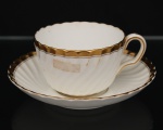 Minton, Staffordshire - Inglaterra. Excepcional xícara para chá em porcelana inglesa da década de 1950, padrão Gold Rose. Esmaltagem vítrea de tom branco perolado, realçado por profusa ornamentação com faixas e filetes à ouro, fundo interno contendo flor em reserva. Bojo aproximadamente obcônico com alça lateral em voluta, assente sobre base circular, ricamente modelado com frisos em espiral relevados na própria pasta; padrão decorativo replicado no pires. Marca da manufatura no verso. Medidas: Xícara: Altura: 5,5 x Comprimento: 11 x Largura: 9 cm; Pires: Diâmetro: 14 cm.