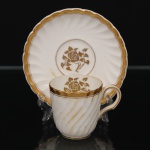 Minton, Staffordshire - Inglaterra. Excepcional xícara para café em porcelana inglesa da década de 1950, padrão Gold Rose. Esmaltagem vítrea de tom branco perolado, realçado por profusa ornamentação com faixas e filetes à ouro, fundo interno contendo flor em reserva. Bojo aproximadamente cilíndrico com alça lateral em voluta, ricamente modelado com frisos em espiral relevados na própria pasta; padrão decorativo replicado no pires. Marca da manufatura no verso. Medidas: Xícara: Altura:  x Comprimento:  x Largura:  cm; Pires: Diâmetro:  cm; Prato: Diâmetro: 17,5 cm. Apresenta marcas de uso e do tempo, vide foto.