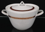 Porcelana, Steatita e Magnésia S/A, Campo Largo - PR(Fundada em 1954). Elegante sopeira em porcelana nacional da década de 1960/70, estilo Art Déco; esmaltagem vítrea na cor branca, decorada por faixa de tonalidade bordô, ornamentada por arabescos fitomorfos dourados em repetição, cercado por frisos em douradura, distribuídos ao redor do bojo e na tampa, pega e alças laterais estilizadas. Marca da manufatura ao fundo. Medidas: Alt.: 17 x Comp.: 27 x Larg.: 21 cm.