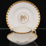 Minton, Staffordshire - Inglaterra. Excepcional trio para chá em porcelana inglesa da década de 1950, padrão Gold Rose. Esmaltagem vítrea de tom branco perolado, realçado por profusa ornamentação com faixas e filetes à ouro, fundo interno contendo flor em reserva. Bojo aproximadamente obcônico com alça lateral em voluta, assente sobre base circular, ricamente modelado com frisos em espiral relevados na própria pasta; padrão decorativo replicado no pires. Marca da manufatura no verso. Medidas: Xícara: Altura: 5,5 x Comprimento: 11 x Largura: 9 cm; Pires: Diâmetro: 14 cm; Prato: Diâmetro: 17,5 cm.