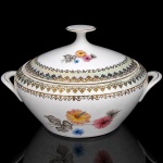 Porcelana Real, Mauá - SP(Fundada em 1943 por Fritz Erwin Schmidt). Elegante sopeira em porcelana nacional da década de 1950/60; esmaltagem vítrea na cor branca, orla circundada por faixa de acabamento nacarado, sobreposta por barrado contínuo de leques estilizados, guirlandas e frisos em douradura, dotado de bela composição botânica em estampagem policromada, predominando as tonalidades preta, rosa, azul e amarelo. Marca manufatura no verso. Medida: Alt.: 17 x Comp.: 27 x Larg.: 22 cm. Apresenta pequeno bicado na pega, e leves desgastes na douradura.