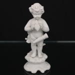 Escultura em porcelana de biscuit representando putto em pé junto a tronco estilizado, segurando coração flamejante nas mãos, com aljava suspensa ao corpo, sobre base moldada de contorno movimentado. Produção decorativa europeia, final do século XIX ou início do século XX. Estado de conservação com desgastes de uso, pequenas manchas e leves sinais do tempo. Condição conforme fotografias. Medidas: Alt.: 13,5 x Diam.: 6 cm.