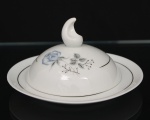 Porcelana Schmidt - Brasil(Fundada em 1945). Manteigueira em porcelana nacional, esmaltagem vítrea na cor branca, dotado de rica decoração com padrão de flores em estampagem, predominando as tonalidades azul, cinza e preto, realçado com frisos em douradura; tampa abaulada encimada por pega com feitio de chama estilizada, presentoir circular. Marca da manufatura ao fundo. Medidas: Alt.: 8,5 x Diam.: 16 cm. Apresenta ínfimo bicado na borda do presentoir.