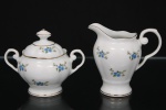 Porcelana Real, Mauá - SP(Fundada em 1943 por Fritz Erwin Schmidt). Uma(01) leiteira e um(01) açucareiro em porcelana nacional da década de 1950/60; esmaltagem vítrea na cor branca, dotada de rica decoração com flores soltas em estampagem policromada, predominando as tonalidades azul e verde, bordas e contornos realçados por friso em douradura; bojo oval assente sobre base circular elevada, borda recortada, tampa ligeiramente abaulada encimada por pega com feitio de pião, alça lateral em voluta, bico vertedor ondulado. Marca da manufatura ao fundo. Medidas: Leiteira: Alt.:  10,5 x Comp.: 11 x Larg.: 8 cm. ; Açucareiro: Alt.: 9 x Comp.: 12 x Larg.: 9 cm.