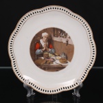 Prato decorativo em porcelana alemã Bavaria, borda recortada com galeria vazada e contornada por filetes dourados, apresentando reserva central com cena que retrata a pintura "Velha Dizendo Graça" (também conhecida como "A Oração sem Fim") do artista holandês Nicolaes Maes, criada por volta de 1656. Produção alemã, marca Bavaria no reverso. Medida: Diam.: 20 cm.