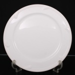 Prato de servir em porcelana branca, formato circular com aba larga decorada por frisos em relevo geométrico distribuídos junto à borda. Medida: Diam.: 32,5 cm.