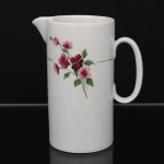Porcelana Renner, Porto Alegre - RS(Fundada em 1937). Leiteira em porcelana nacional da década de 1960/70, série "Medaillon"; esmaltação branca, decorada por composição floral em estampagem policromada, cercada por friso em douradura. Bojo cilíndrico, bico vertedor revirado para fora, alça lateral curvada. Marcada da manufatura ao fundo. Medidas: Alt.: 17,5 x Comp.: 15,5 x Larg.: 9 cm.
