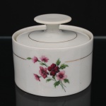 Porcelana Renner, Porto Alegre - RS(Fundada em 1937). Açucareiro em porcelana nacional da década de 1960/70, série "Medaillon"; esmaltação branca, decorada por composição floral em estampagem policromada, cercada por friso em douradura. Bojo cilíndrico tampa encimada por puxador circular. Marcada da manufatura ao fundo. Medidas: Alt.: 9,5 x Diam.: 11,5 cm.