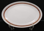 Porcelana, Steatita e Magnésia S/A, Campo Largo - PR(Fundada em 1954). Elegante travessa oval em porcelana nacional da década de 1960/70; esmaltagem vítrea na cor branca, orla decorada por faixa de tonalidade bordô, ornamentada por arabescos fitomorfos dourados em repetição, cercado por frisos em douradura. Marca da manufatura no verso. Medidas: Comp.: 37 x Larg.: 24 cm.
