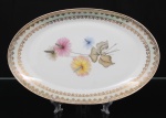 Porcelana Real, Mauá - SP(Fundada em 1943 por Fritz Erwin Schmidt). Travessa oval em porcelana nacional da década de 1950/60; esmaltagem vítrea na cor branca, orla circundada por faixa de acabamento nacarado, sobreposta por barrado contínuo de leques estilizados, guirlandas e frisos em douradura, centro dotado de bela composição botânica em estampagem policromada, predominando as tonalidades preta, rosa, azul e amarelo. Marca manufatura no verso. Medidas: Comp.: 31,5 x Larg.: 20 cm.
