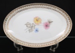Porcelana Real, Mauá - SP(Fundada em 1943 por Fritz Erwin Schmidt). Elegante travessa oval em porcelana nacional da década de 1950/60; esmaltagem vítrea na cor branca, orla circundada por faixa de acabamento nacarado, sobreposta por barrado contínuo de leques estilizados, guirlandas e frisos em douradura, centro dotado de bela composição botânica em estampagem policromada, predominando as tonalidades preta, rosa, azul e amarelo. Marca manufatura no verso. Medida: Comp.: 35,5 x Larg.: 23 cm.