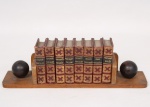 Conjunto de oito minidicionários de bolso encadernados, reunindo traduções entre os idiomas português, inglês, francês, espanhol e italiano, com lombadas decoradas em douração. Acompanhados de porta-livros em madeira com terminais esféricos. Exemplares impressos em papel, com encadernação em percalina vermelha. Apresentam desgastes, perdas e marcas de uso compatíveis com a antiguidade. Medidas porta-livro: Alt.: 5 x Comp.: 18 x Larg.: 6,5 cm. ; Medidas livros: Alt.: 2 x Comp.: 7,5 x Larg.: 5 cm.