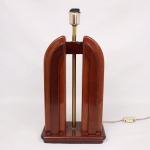 Abajur de mesa de desenho Art Déco, estruturado em madeira de tonalidade castanho-avermelhada, composta por elementos arqueados simétricos sobre base retangular escalonada. Haste central em metal dourado sustentando soquete elétrico. Identificado por plaqueta frontal com a inscrição Della Robbia. Apresenta sinais de uso, desgastes compatíveis com o tempo, ausência da cúpula e avarias no soquete. Peça eletrificada. Medidas: Alt.: x Comp. x Larg.: