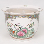 Cachepot em porcelana chinesa, decoração policroma esmaltada representando personagens em jardim com pinheiro, aves, flores e frutos, reservada por cercaduras florais e elementos ornamentais, realçados por filetes dourados. Corpo de formato campanular com borda alargada. Medidas: Alt.: 18 x Diam.: 24 cm.