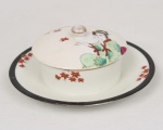 Mateigueira em porcelana japonesa, formato circular fixada sobre presentoir, tampa ligeiramente abaulada encimada por pega de forma arredondada. Decoração policromada representando figura feminina em trajes tradicionais japoneses, acompanhada por ramos de folhas estilizadas. Borda realçada por friso em tonalidade preta e contorno com filete dourado. Base marcada com inscrição Made in Japan. Medidas: Alt.: 5 x Diam.: 14,5 cm.