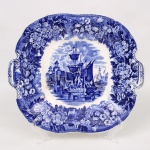 Travessa de servir em faiança inglesa Wedgwood, modelo com alças laterais integradas, decorada em estampagem monocromática azul sob esmalte, apresentando reserva central com cena portuária composta por embarcações e arquitetura fortificada, circundada por cercadura floral. Marca da manufatura Wedgwood, Etruria, England, na base. Medidas: Comp.; 26,5 x Larg.: 23 cm.