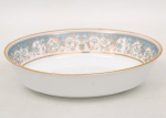 NORITAKE, Nagoya - Japão(Fundada em 1904 pelos irmãos Ichizaemon e Toyo Morimura). Exuberante travessa funda em porcelana da década de 1960/70, padrão POLONAISE (2045); Formato oval, raso, de centro ligeiramente rebaixado. Aba profusamente ornamentada por composição vegetalista, composta por rinceau, volutas, ramos, folhas e flores dispostas em repetição, sobre cartela de tonalidade azul ciano, seguindo repertório derivado de padrões europeus, estilo neoclássico e revivalista; contornos e elementos internos definidos por generosa aplicação de filetes à ouro, incluindo a borda e o centro. Marca da manufatura no verso. Medidas: Alt.: 6,5 x Comp.: 25 x Larg.: 19 cm.