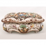Caixa de porcelana italiana Capodimonte, de formato retangular com contornos recortados, apoiada sobre pés integrados, apresentando decoração moldada em relevo de volutas, folhagens e reservas com cenas galantes e pastorais compostas por figuras femininas, masculinas e putti. Tampa basculante ornada por composição central figurativa em relevo policromado, centralizada por elementos rocaille. Interior decorado com ramalhetes florais esmaltados. Base marcada sob vidrado com brasão e inscrição R. Capodimonte, acompanhada da numeração 3779 e indicação de procedência italiana. Apresenta quebraduras, trincados e partes coladas, demanda grande restauro. Medidas: Alt.: 17 x Comp.: 35 x Larg.: 23 cm.