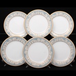 NORITAKE, Nagoya - Japão(Fundada em 1904 pelos irmãos Ichizaemon e Toyo Morimura). Exuberante conjunto de pratos rasos para jantar em porcelana da década de 1960/70, padrão POLONAISE (2045); esmaltagem vítrea na cor branca, aba profusamente ornamentada por composição vegetalista, composta por rinceau, volutas, ramos, folhas e flores dispostas em repetição, sobre cartela de tonalidade azul ciano, seguindo repertório derivado de padrões europeus, estilo neoclássico e revivalista; borda e caldeira circundadas generosa aplicação de filetes à ouro. Marca da manufatura no verso. Composto de seis(06) unidades. Medida: Diam.: 26,8 cm.