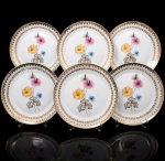 Porcelana Real, Mauá - SP(Fundada em 1943 por Fritz Erwin Schmidt). Elegante conjunto de pratos rasos em porcelana nacional da década de 1950/60; esmaltagem vítrea na cor branca, orla circundada por faixa de acabamento nacarado, sobreposta por barrado contínuo de leques estilizados, guirlandas e frisos em douradura, centro dotado de bela composição botânica em estampagem policromada, predominando as tonalidades preta, rosa, azul e amarelo. Marca manufatura no verso. Composto de seis(06) unidades. Medida: Diam.: 25 cm.