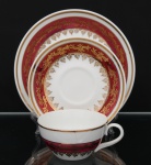 Porcelana Schmidt - Brasil(Fundada em 1945). Belíssimo trio para chá em porcelana nacional da década de 1960/70; bojo hemisférico e alça lateral curvada, esmaltagem vítrea na cor branca, decorado com faixas de tom rubi e ornamentação em douradura aplicada, formando cercaduras de arabescos, elementos fitomorfos e rendilhados estilizados; bordas contornadas por filetes à ouro, padrão decorativo integralmente replicado no pires e no prato. Marca da manufatura no verso. Medidas: Xícara: Alt.: 5 x Comp.: 12 x Larg.: 9,5 cm. ; Pires: Diam.: 14,5 cm. ; Prato: Diam.: 19 cm.