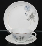 Porcelana Schmidt - Brasil(Fundada em 1945). Trio para chá em porcelana nacional, esmaltagem vítrea na cor branca, dotado de rica decoração com padrão de flores em estampagem, predominando as tonalidades azul, cinza e preto, realçado com frisos em douradura; bojo hemisférico e alça lateral em voluta. Padrão decorativo replicado no pires e no prato. Marca da manufatura ao fundo.  Medidas: Xícara: Alt.:5 x Comp.: 12 x Larg.: 9,5 cm. ; Pires: Diam.: 14 cm. ; Prato: 18,5 cm.