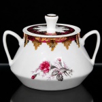 Porcelana Schmidt - Brasil(Fundada em 1945). Açucareiro em porcelana nacional da década de 1960/70; esmaltação branca, decorado com reservas florais em policromia representando rosas e botões, complementadas por folhagens em tons de cinza, borda ornamentada com faixa de tonalidade bordô e elementos rendilhados aplicados em douradura; bojo cônico, tampa removível encimada por pega obcônica, alças laterais estilizadas. Marca da manufatura ao fundo. Medidas: Alt.: 8,5 x Comp.: 12 x Larg.: 10 cm.