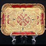 Bandeja veneziana retangular de madeira entalhada e policromada, com decoração em relevo composta por volutas, folhagens estilizadas e motivo central simétrico de inspiração barroca. Superfície com acabamento dourado e detalhes em vermelho e preto. Bordas recortadas e molduradas em relevo. Apresenta desgaste, perdas de policromia e marcas compatíveis com o uso e o tempo. Medidas: Alt.: x Comp.: