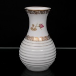 Porcelana Real, Mauá - SP(Fundada em 1943 por Fritz Erwin Schmidt). Vaso em porcelana nacional, esmaltação branca, corpo torneado com bojo canelado e colo expandido. Decoração composta por friso floral em douração, reserva com botão de rosa e filetes aplicados na borda e na transição do corpo. Marca da manufatura ao fundo. Medidas: Alt.: 19 x Diam.: 12 cm.