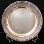FRACALANZA. Elegante bandeja confeccionada em metal espessurado à prata, formato circular, centro ligeiramente rebaixado, borda relevada com fileira de frisos intercaladas por fitas cruzadas, ornato obtido através da técnica do cinzelado. Marca da manufatura no verso. Apresenta marcas de uso. Medida: Diam.: 30,5 cm. Necessita apenas polimento.