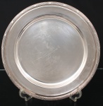 FRACALANZA. Elegante bandeja confeccionada em metal espessurado à prata, formato circular, centro ligeiramente rebaixado, borda relevada com fileira de frisos intercaladas por fitas cruzadas, ornato obtido através da técnica do cinzelado. Marca da manufatura no verso. Apresenta marcas de uso. Medida: Diam.:  36 cm. Apresenta marcas de uso.