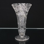 Vaso em cristal incolor lapidado, de corpo obcônico e pé circular. Decorado com reservas geométricas, motivos estrelados, losangulares e facetados, apresentando borda recortada. Acompanha acentuada rachadura. Medidas: Alt.: 19,5 x Diam.: 11 cm.
