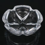 Cinzeiro em cristal incolor moldado, de formato lobado, com quatro apoios para cigarro integrados à borda. Corpo de desenho orgânico com reservas côncavas e base espessa. Medidas: Diam.: 11,5 cm.