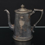 Bule para café em metal prateado, corpo cilíndrico, tampa articulada por dobradiça, bico vertedor curvo e pega estilizada. Decorado com brasão gravado em reserva. Base marcada R. Wallace, modelo 0376R, inscrição Silver Soldered 16 oz.. Necessita polimento e/ou refazer banho de prata. Medidas: Alt.: 15 x Comp.: 18,5 x Larg.: 9,5 cm.