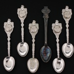 Conjunto composto por cinco colheres decorativas em metal prateado, com cabos vazados em relevo e medalhão representando São Cristóvão, e uma colher de coleção publicitária da relojoaria Bucherer, marcada Rolex Bucherer Genève e Bucherer of Switzerland. Medidas: Comp.: 10 cm.