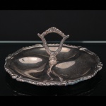 Petisqueira circular em metal prateado, de formato lobulado, dividida em quatro compartimentos, com alça central vazada e decoração em relevo de inspiração rocaille. Necessita apenas polimento. Medidas: Alt.: 10 x Diam.: 20,5 cm.
